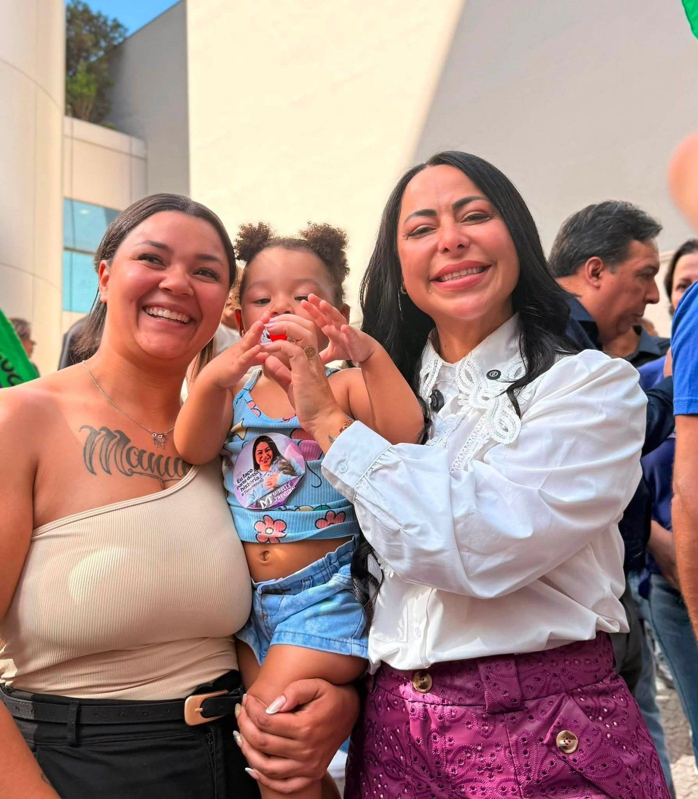 Mirelle Trevisan aparece ao lado de uma mulher e uma criança durante um encontro.