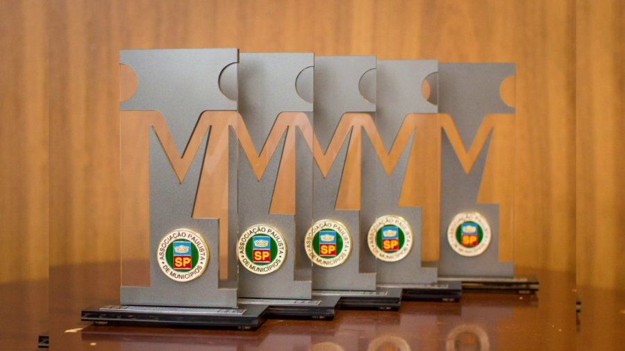 Troféus dourados alinhados sobre uma mesa em cerimônia da Associação Paulista de Municípios.