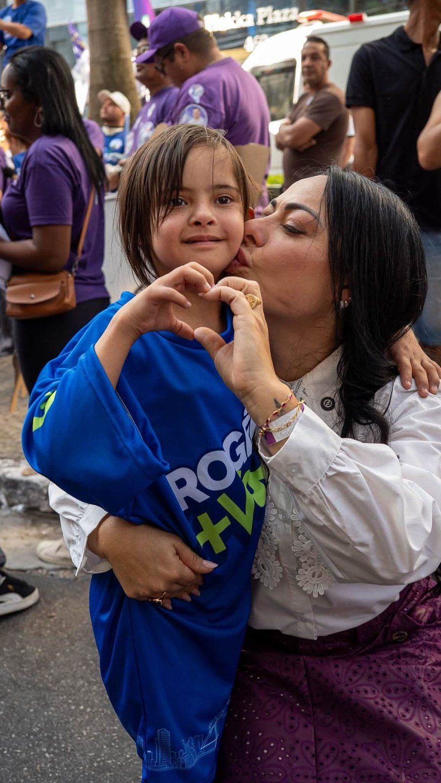 Mirelle Trevisan beija o rosto de uma criança que forma um coração com as mãos.